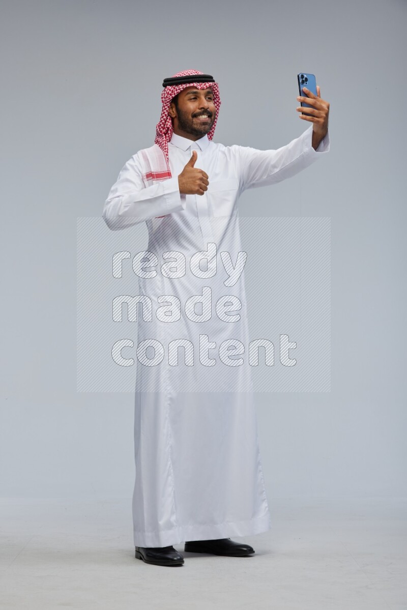 Saudi man Wearing Thob and shomag standing taking selfie on Gray background