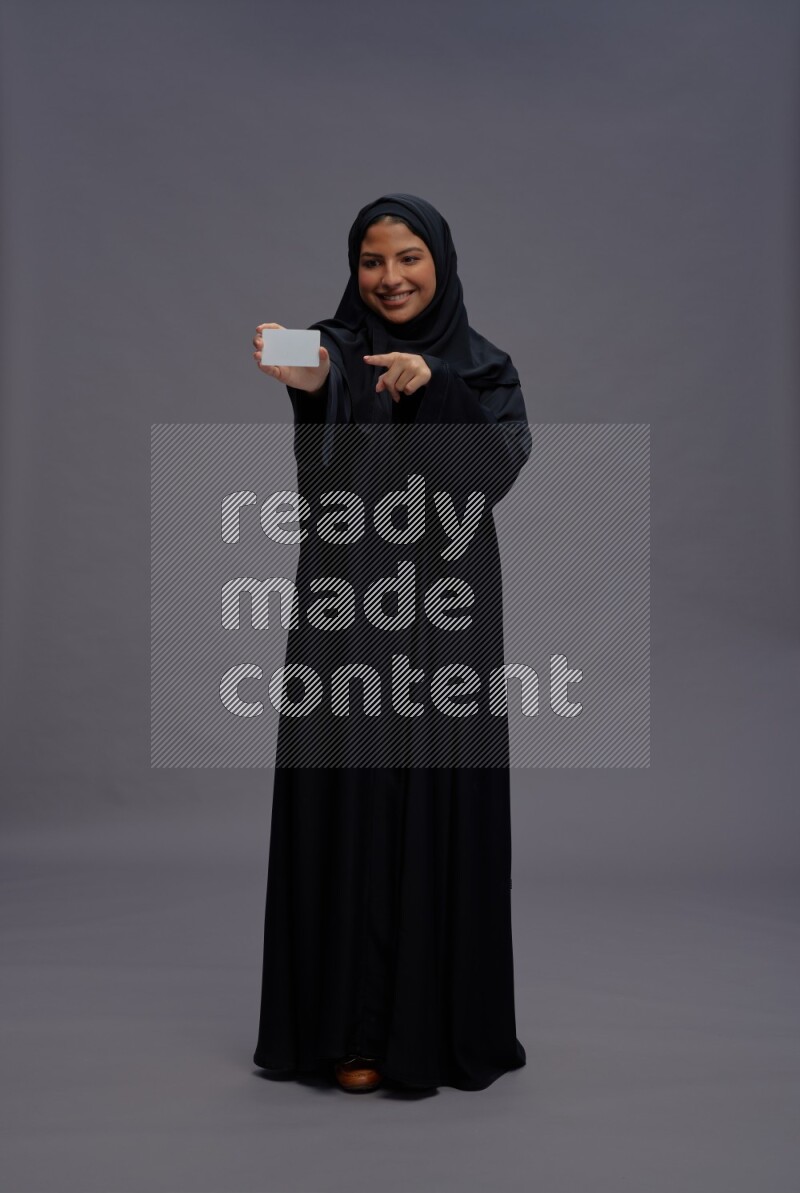 Saudi woman wearing Abaya standing holding ATM card on gray background