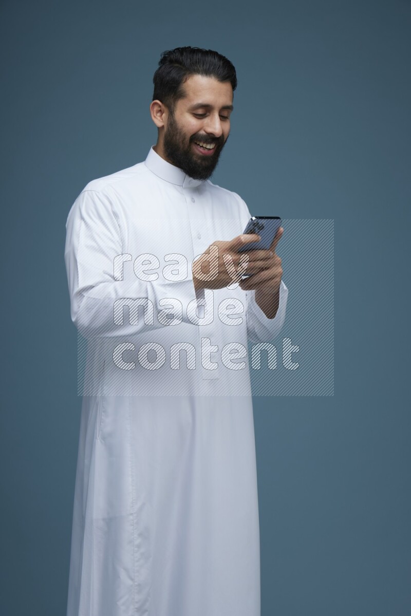 A man Texting in a blue background wearing Saudi Thob