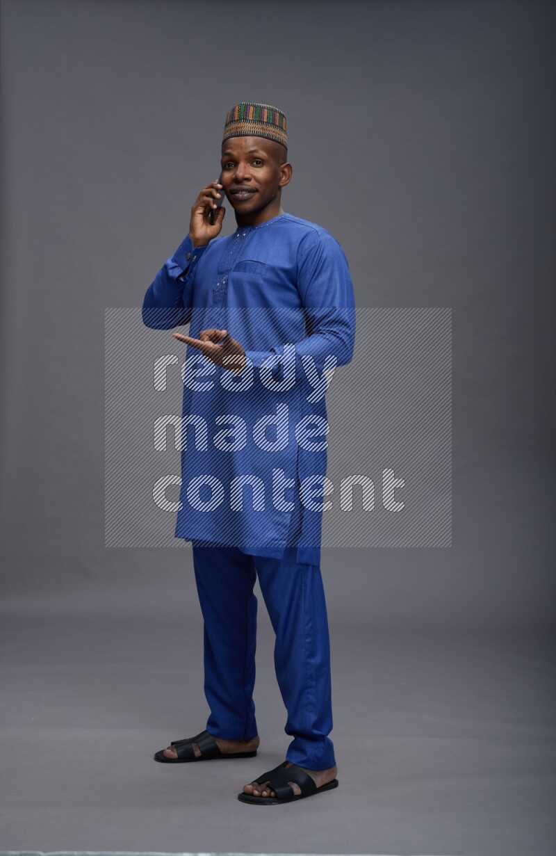 Man wearing Nigerian outfit standing talking on phone on gray background