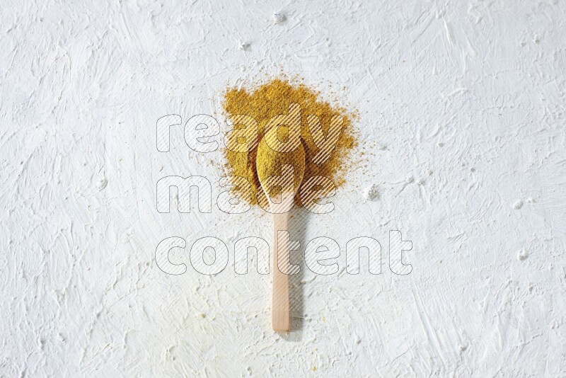 A wooden spoon full of turmeric powder on textured white background