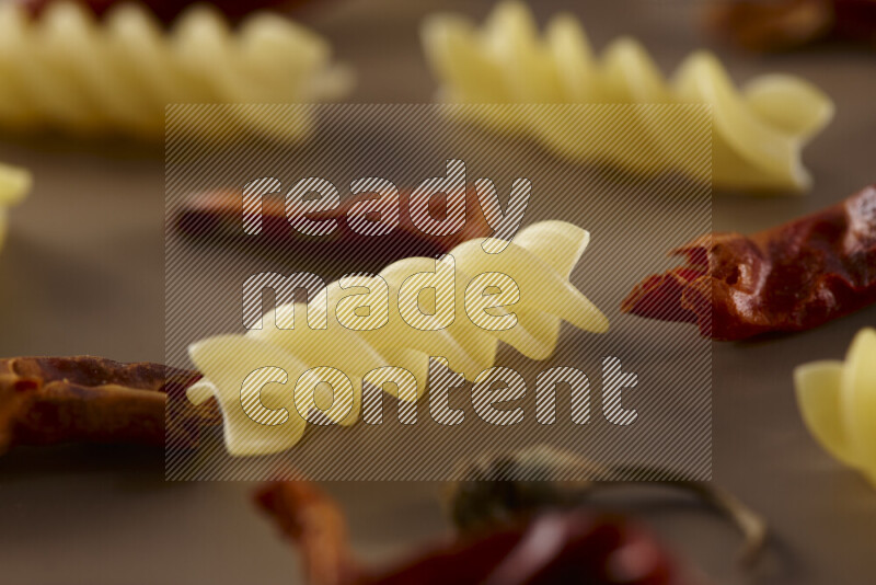 Raw pasta with different ingredients such as cherry tomatoes, garlic, onions, red chilis, black pepper, white pepper, bay laurel leaves, rosemary and cardamom on beige background