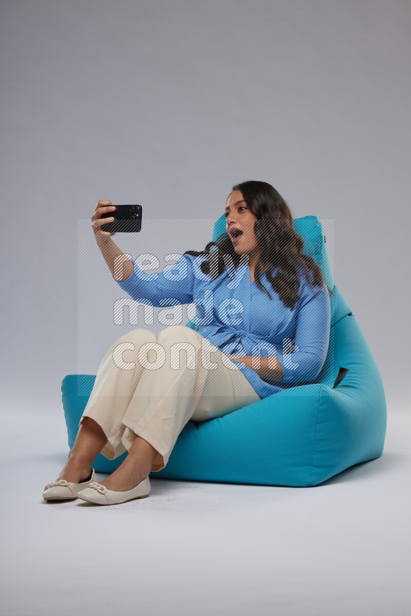 A woman sitting on a blue beanbag and taking selfie