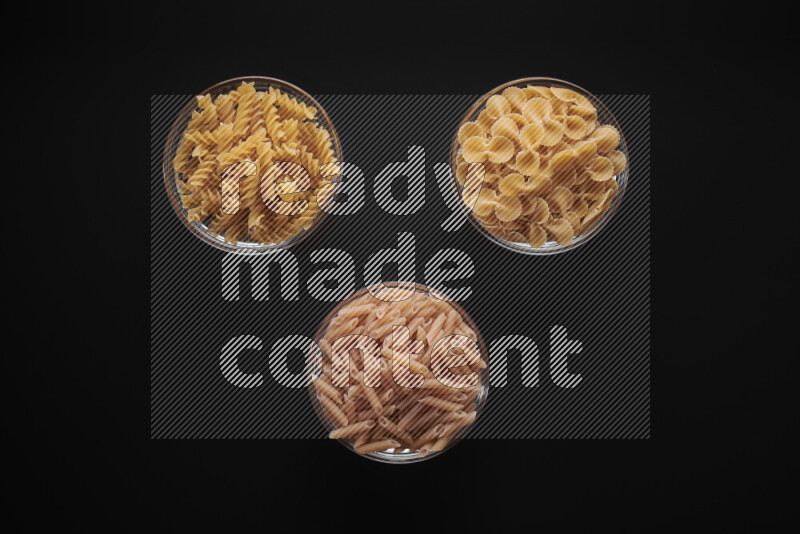 Different pasta types in glass bowls on black background