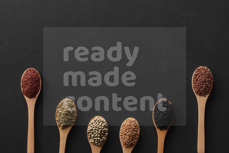 wooden spoons filled with white peppers, mustard seeds, black seeds, garden cress, cumin and flax on black flooring