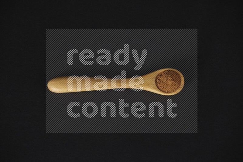 Cinnamon powder in a wooden spoon on a black background
