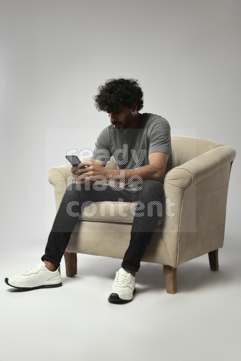 A man wearing casual sitting on a chair texting on the phone on white background