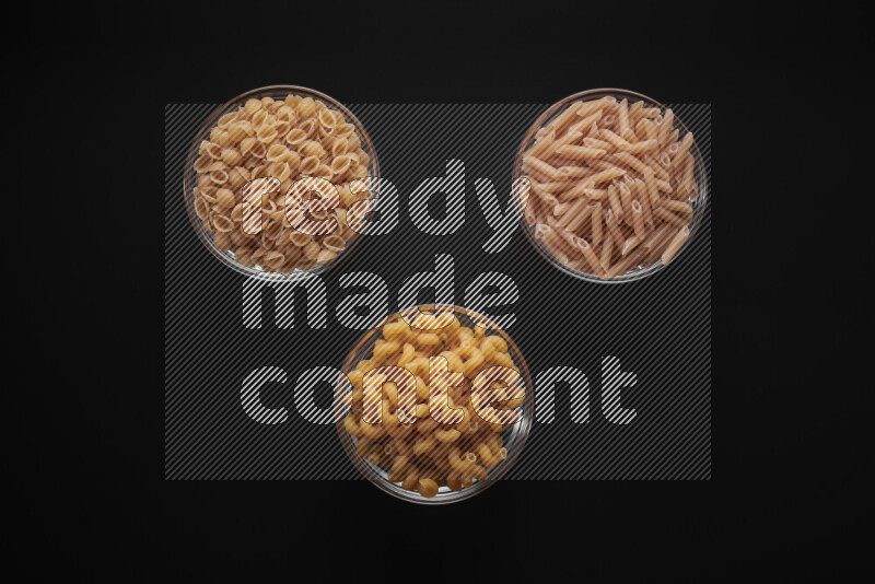 Different pasta types in glass bowls on black background