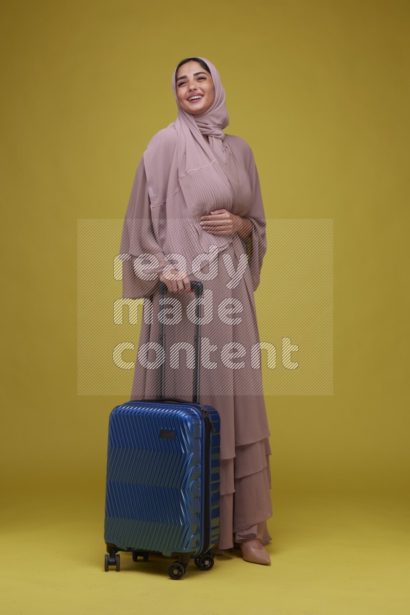 A woman With suit Case on a Yellow Background wearing Brown Abaya with Hijab