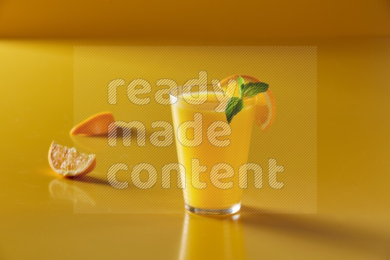glass of orange juice with orange & mint  on yellow background