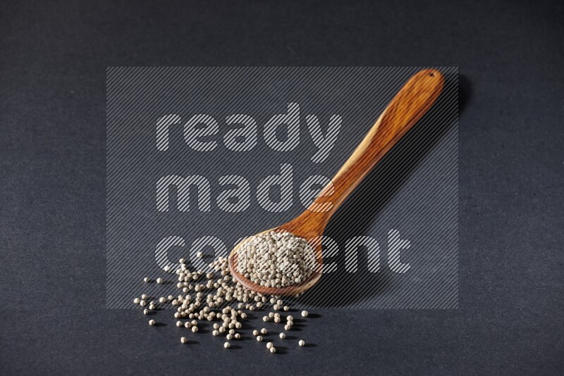 A wooden ladle full of white pepper beads on black flooring