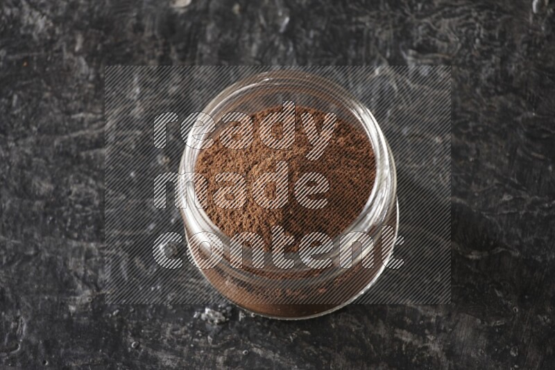 A glass jar full of cloves powder on a textured black flooring
