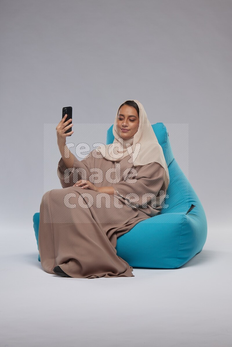 A Saudi woman sitting on a blue beanbag and taking selfie