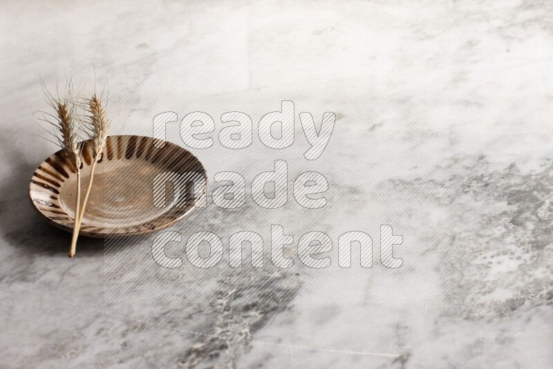 Wheat stalks on multicolored pottery plate on grey marble background
