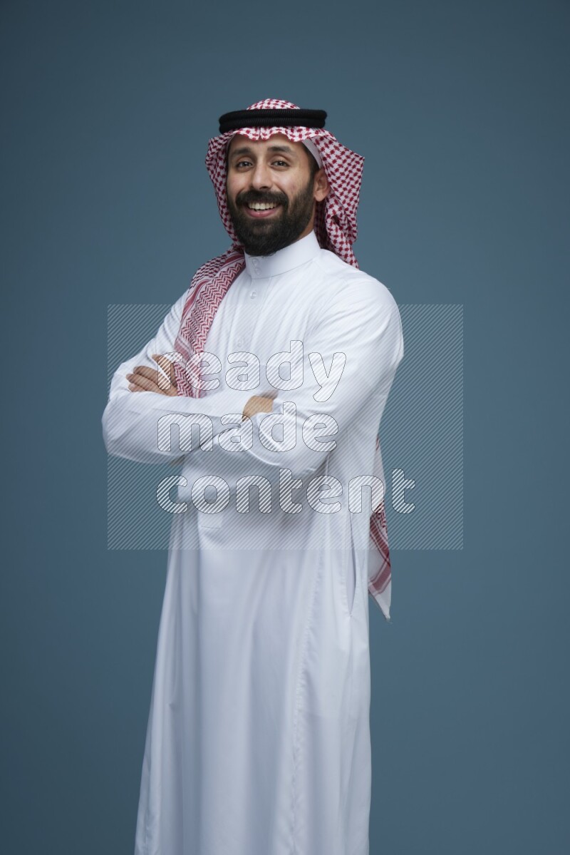 A man posing in a blue background wearing Saudi Thob and Shomag
