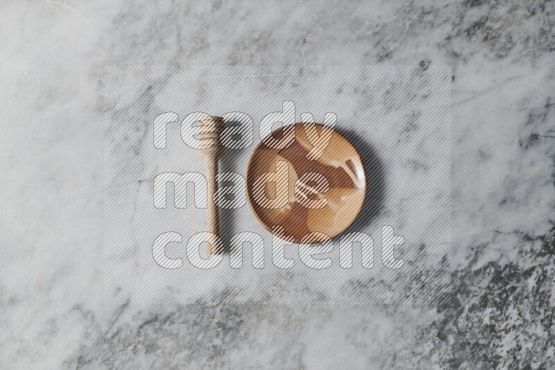 Multicolored pottery plate with wooden honey dipper on the side on grey marble background
