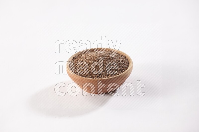 A wooden bowl full of flax seeds on a white flooring