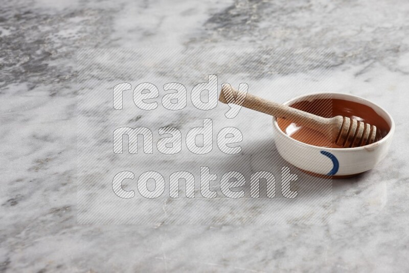 Multicolored pottery bowl with wooden honey dipper in it on grey marble background