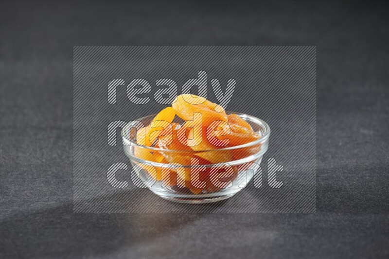 A glass bowl full of dried apricots on a black background in different angles