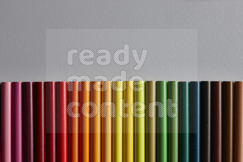 A collection of colored pencils arranged showcasing a gradient of different hues on grey background