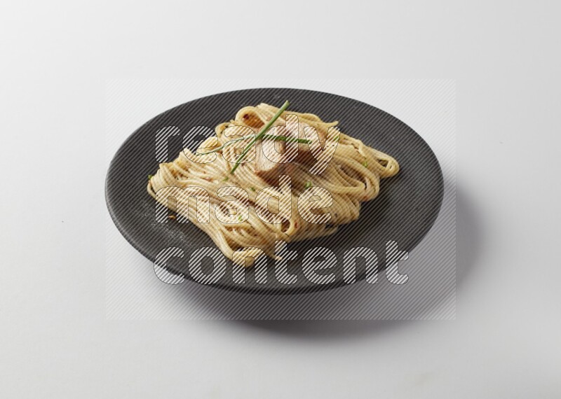 spaghetti pasta with white sauce on a black plate on a white background