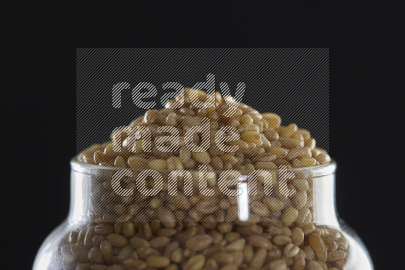 Hulled wheat in a glass jar on black background