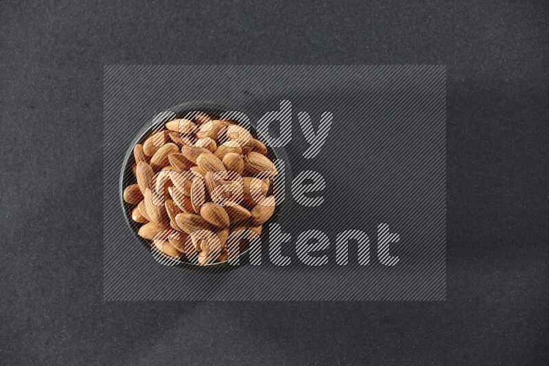 A black pottery bowl full of peeled almonds on a black background in different angles