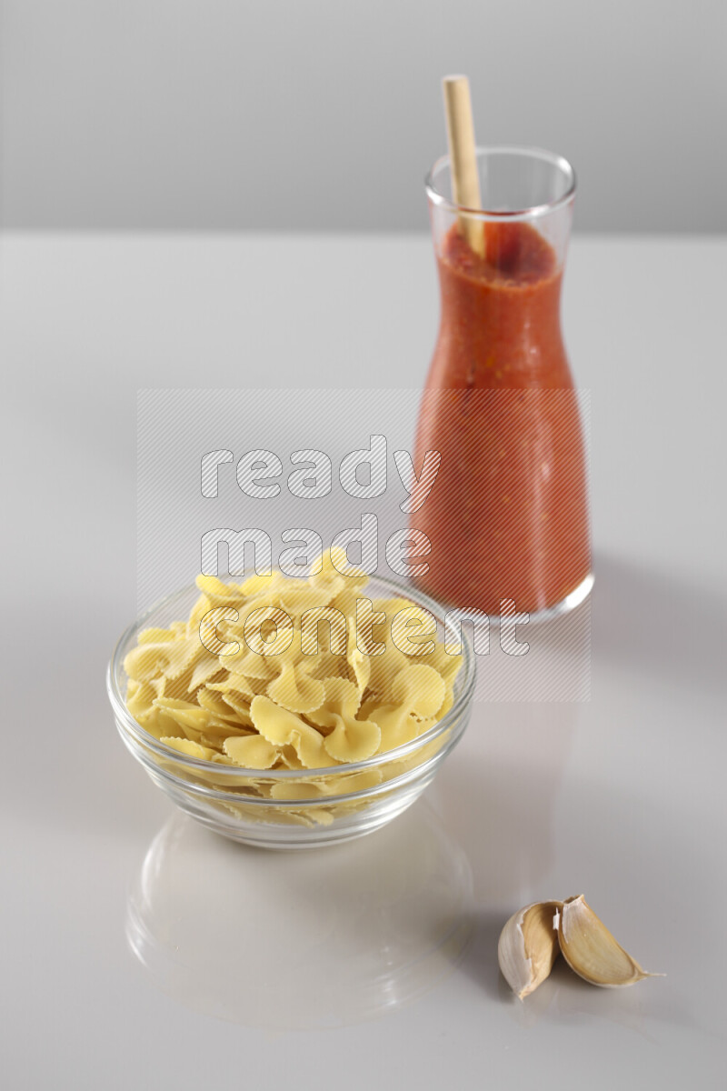 Raw pasta with tomatoe pasta with different ingredients such as cherry tomatoes, basil, garlic, bay laurel, cardamom, white pepper, black pepper, red chilis and wheat stalks on light grey background