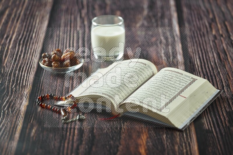 Quran with dates, prayer beads and different drinks all placed on wooden background