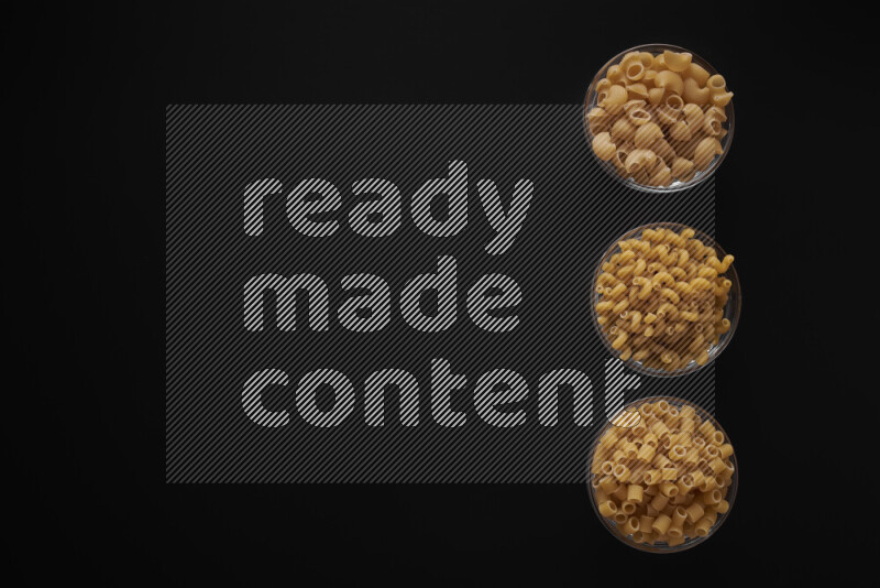 Different pasta types in 3 glass bowls on black background