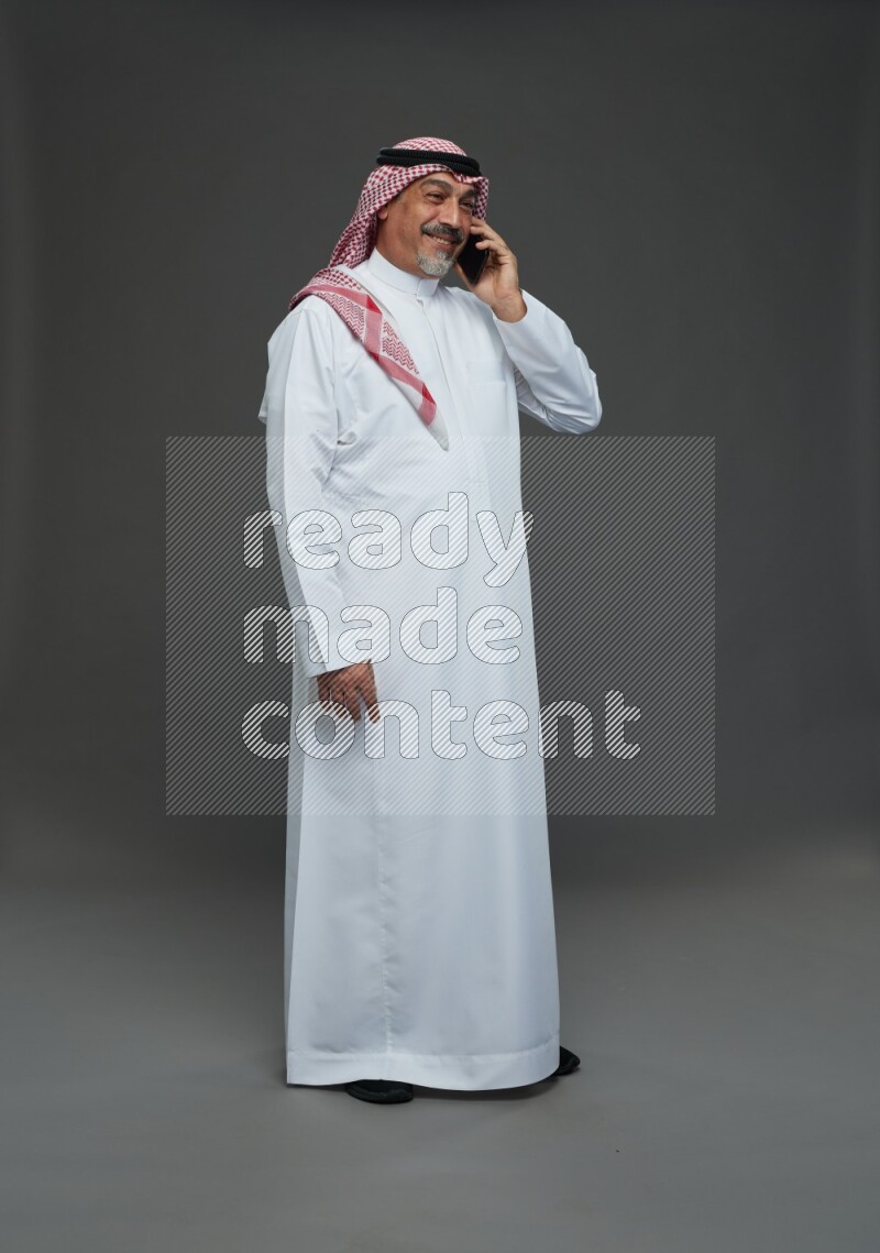 Saudi man with shomag Standing talking on phone on gray background