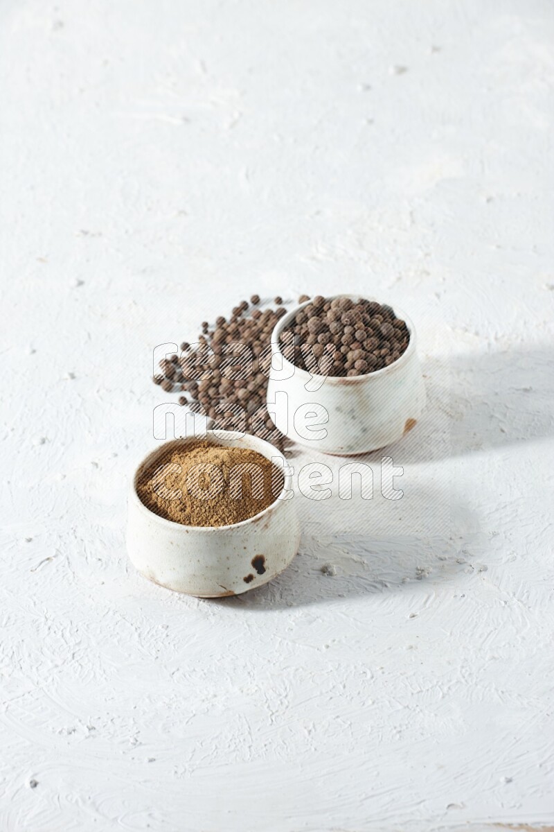 وعاءان بيج، أحدهما ممتلئ ببودرة بهار الفلفل الحلو والآخر بالحبوب مع البودرة والحبوب متناثرة على خلفية بيضاء