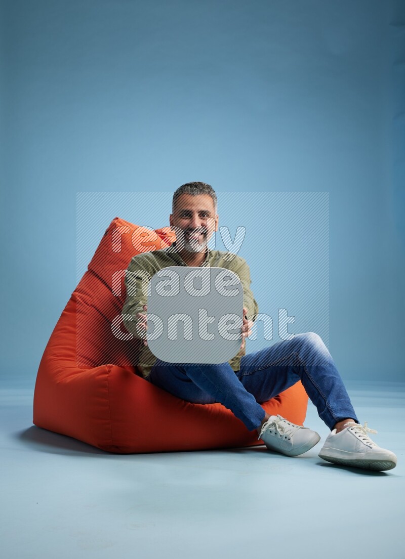 A man sitting on a orange beanbag and holding social media sign