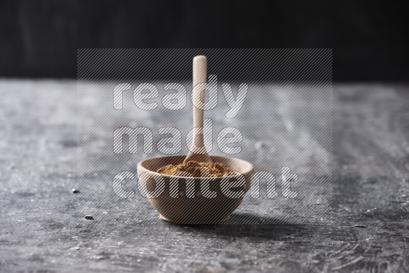 Wooden bowl full of cinnamon powder with a wooden spoon on a textured black background in different angles