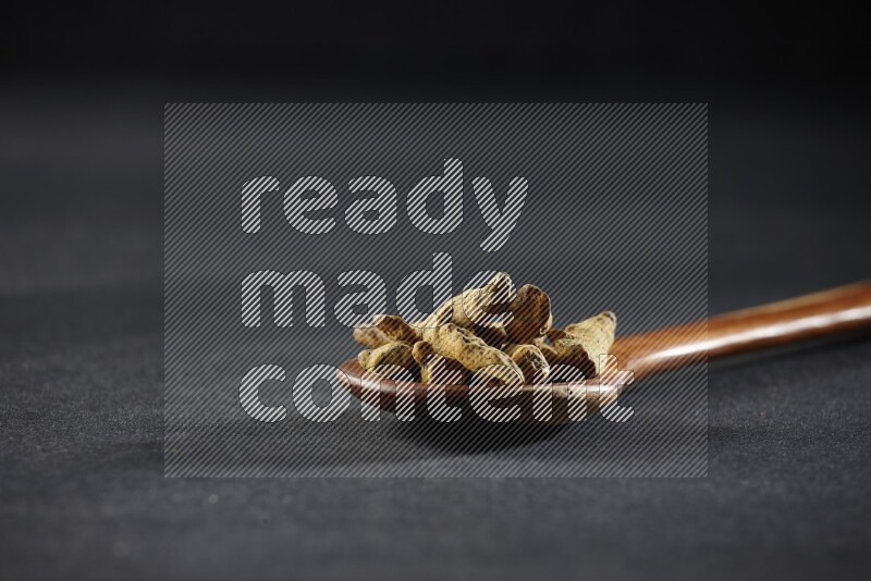 مغرفة خشبية ممتلئة بأصابع الكركم المجففة على خلفية سوداء