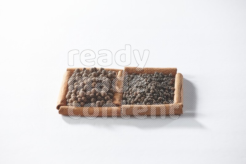 مربعان من أعواد القرفة ممتلئان بحبوب الفلفل الأسود وحبوب الفلفل الحلو علي خلفية بيضاء