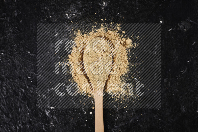 A wooden spoon full of ground ginger powder on black background