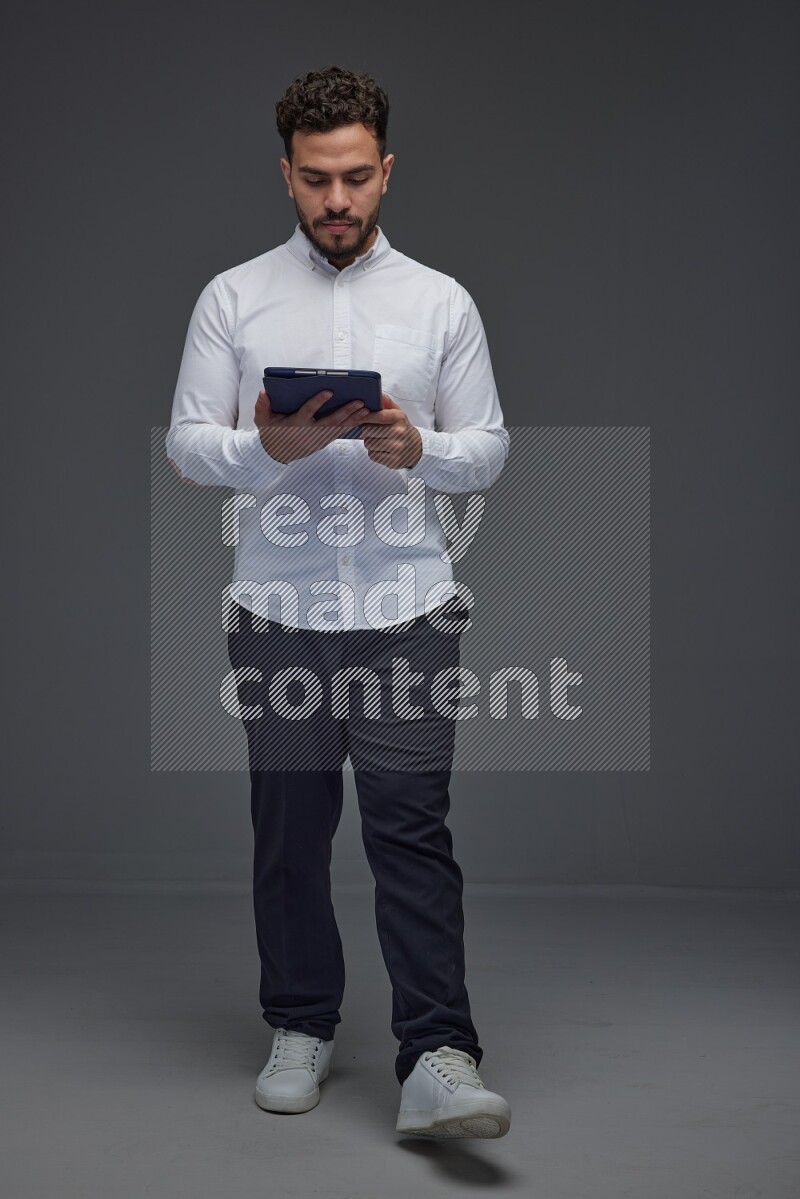 A man wearing smart casual standing and using his tablet eye level on a gray background