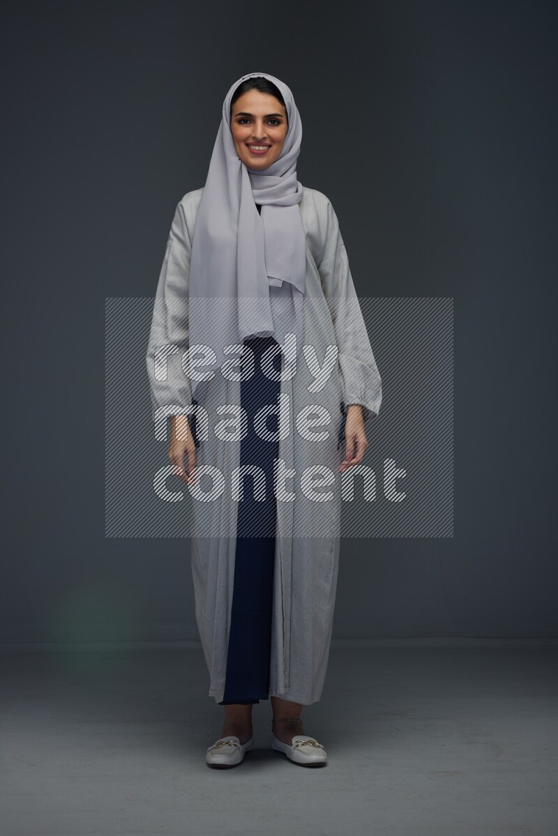 A Saudi woman wearing a light gray Abaya and head scarf standing and making multi poses eye level on a grey background