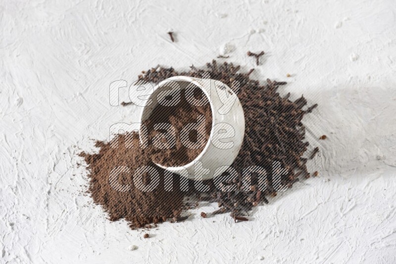 A beige ceramic bowl with cloves powder spilled out of it on a textured white flooring