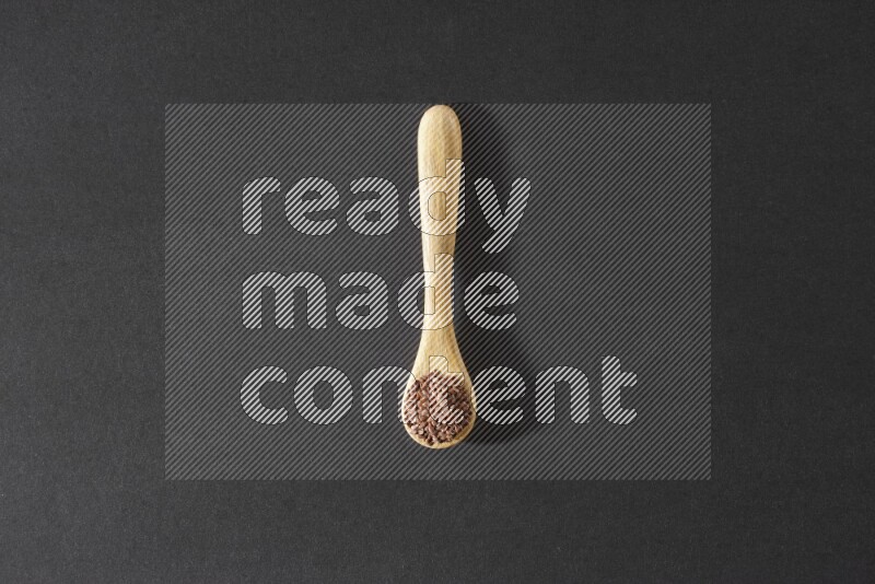 A wooden spoon full of flaxseeds on a black flooring