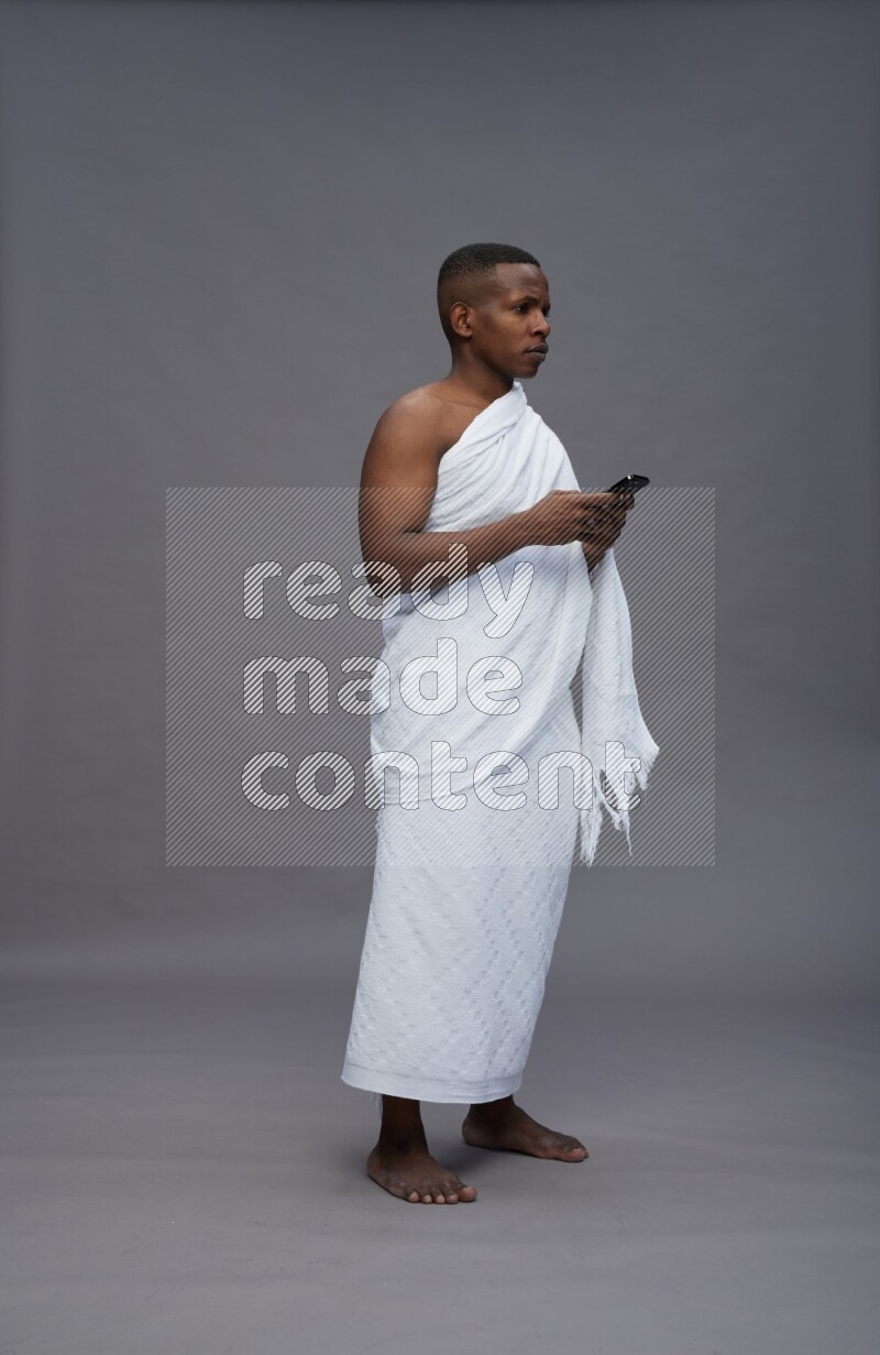 A man wearing Ehram Standing texting on phone on gray background