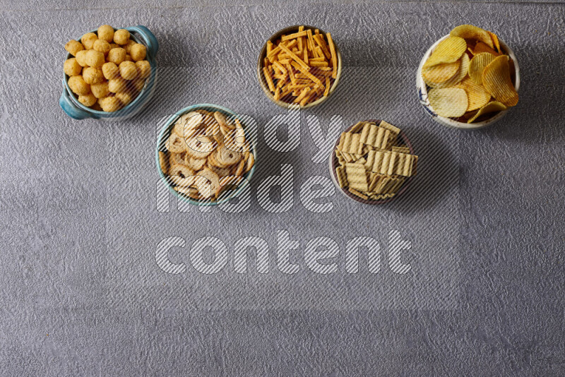 Assorted snacks in pottery bowls on grey background