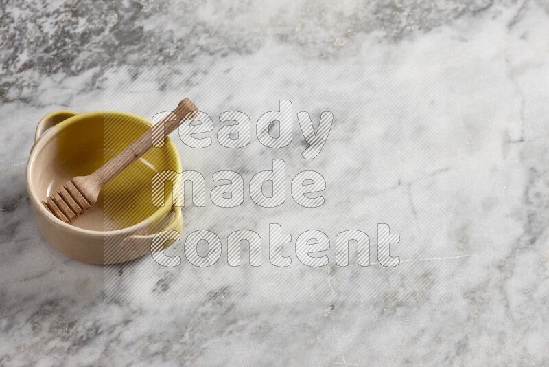 Multicolored pottery bowl with wooden honey dipper in it on grey marble background