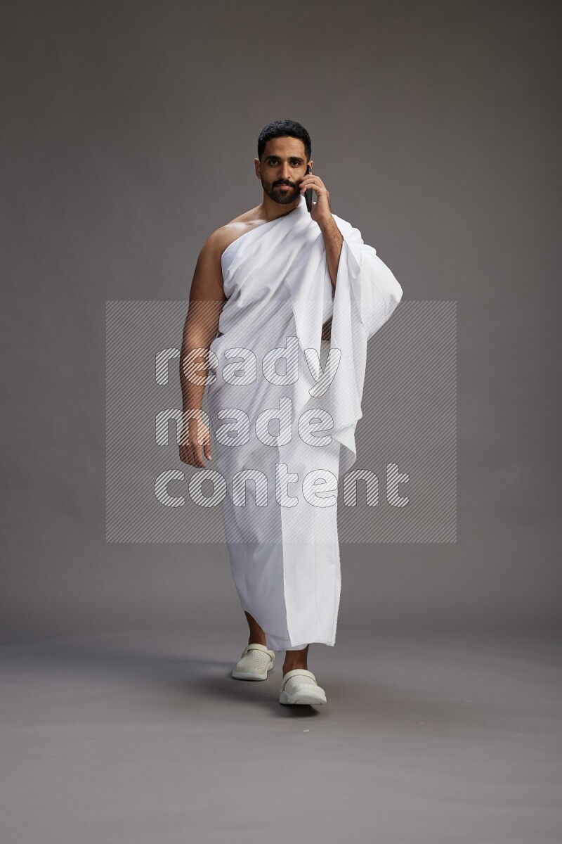 A man wearing Ehram Standing talking on phone on gray background