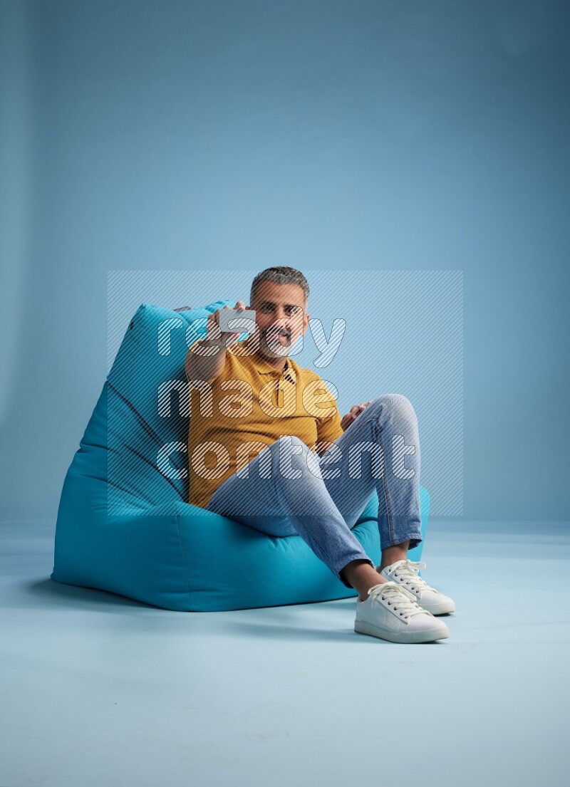 A man sitting on a blue beanbag and holding ATM card