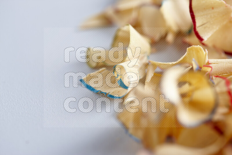 A close-up showing a small pile of pencil shavings with varied color edges on grey background