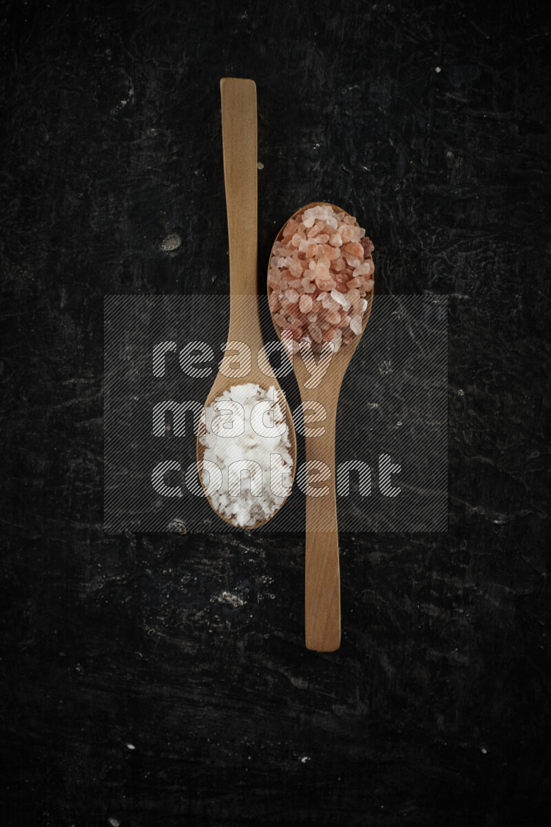 2 wooden spoons filled with fine and coarse salt on black background