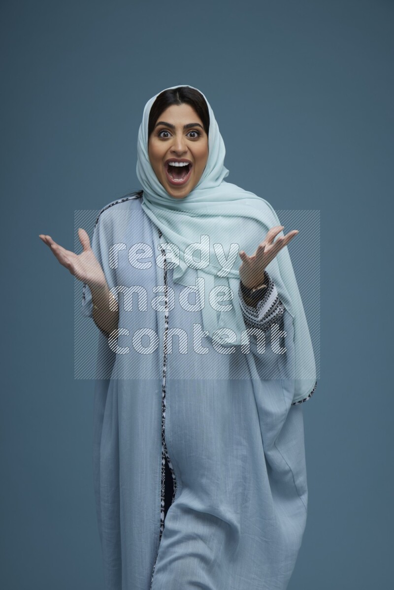 A woman posing in a blue background wearing a blue Abaya with hijab