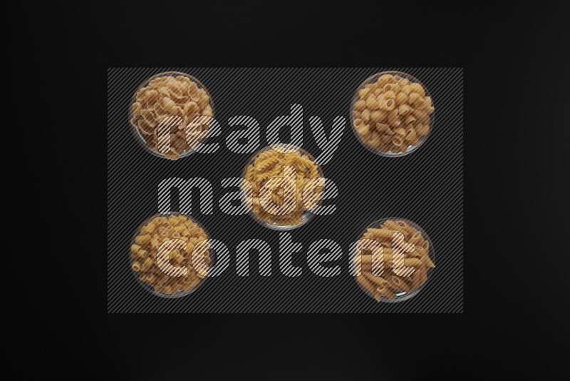 Different pasta types in 5 glass bowls on black background